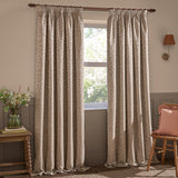 Grace Leaf Jacquard pencil pleat curtains in taupe, shown floor-length either side of a window with a woven leaf pattern, hung from a wooden pole in a living room setting.