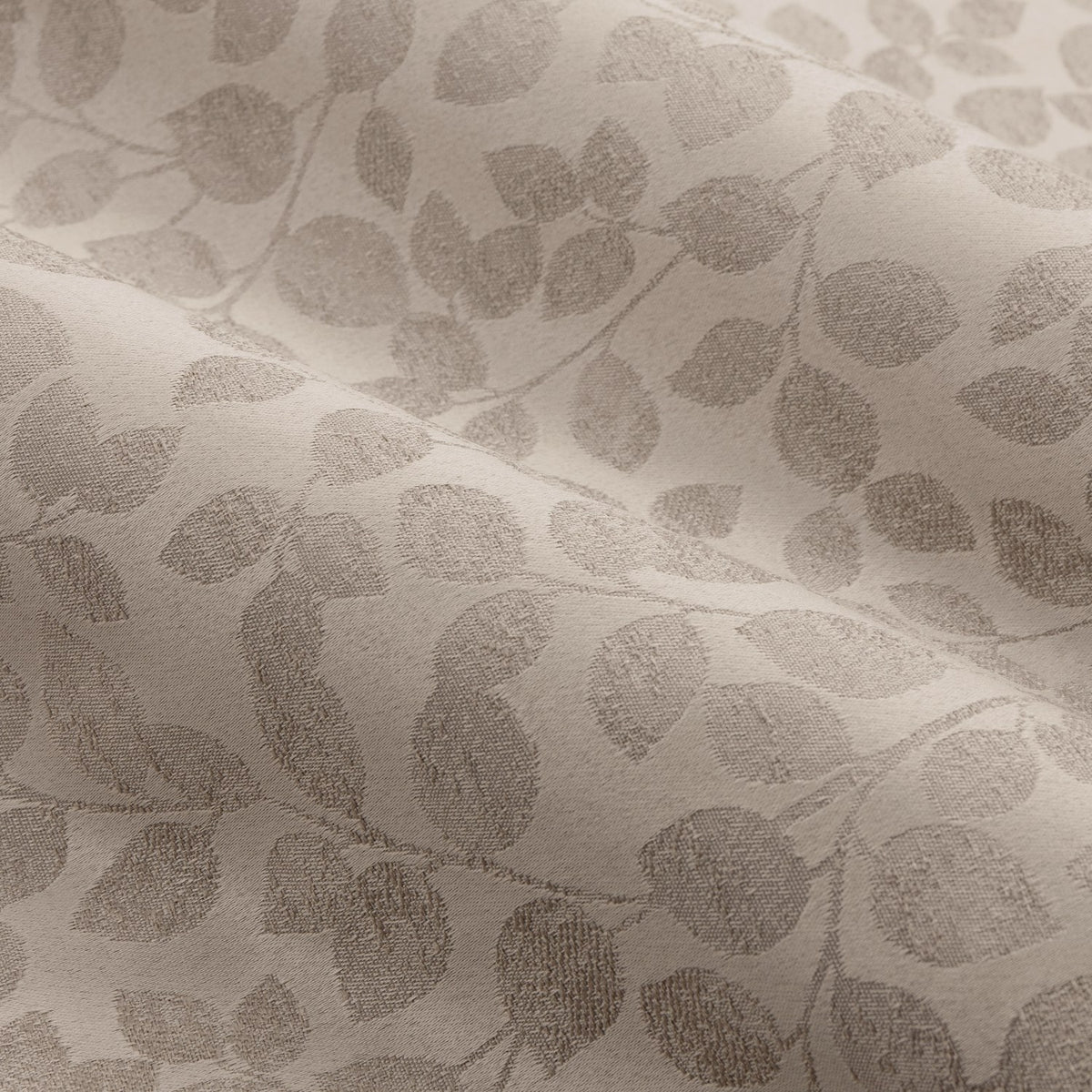 Close-up of Grace Leaf Jacquard pencil pleat curtain fabric in taupe, showing a woven trailing leaf pattern in matt satin polyester with soft folds.
