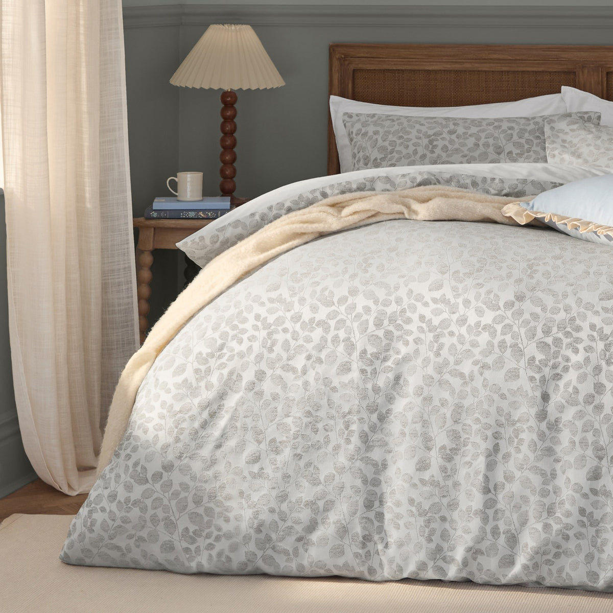 Grace Leaf Jacquard Floral Duvet Cover Set in mist grey, shown on a bedroom bed with matching pillowcases, woven trailing leaf pattern, styled with a cream throw and wooden rattan headboard.