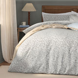 Grace Leaf Jacquard Floral Duvet Cover Set in mist grey, shown on a bedroom bed with matching pillowcases, woven trailing leaf pattern, styled with a cream throw and wooden rattan headboard.