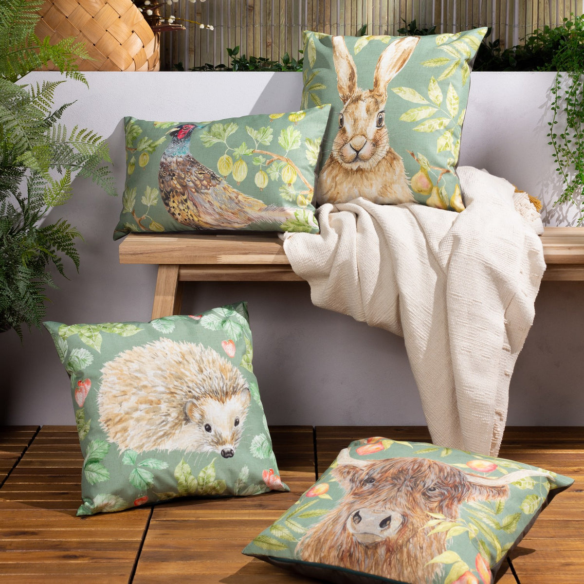 Grove Animal Polyester Cushion in Olive with hedgehog design, shown among matching pheasant, hare and Highland cow cushions on a wooden garden bench.