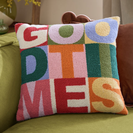 Good Times Tufted Polyester Cushion, a multicoloured 43cm square with "GOOD TIMES" in bold boucle-tufted letters, shown on a green sofa.