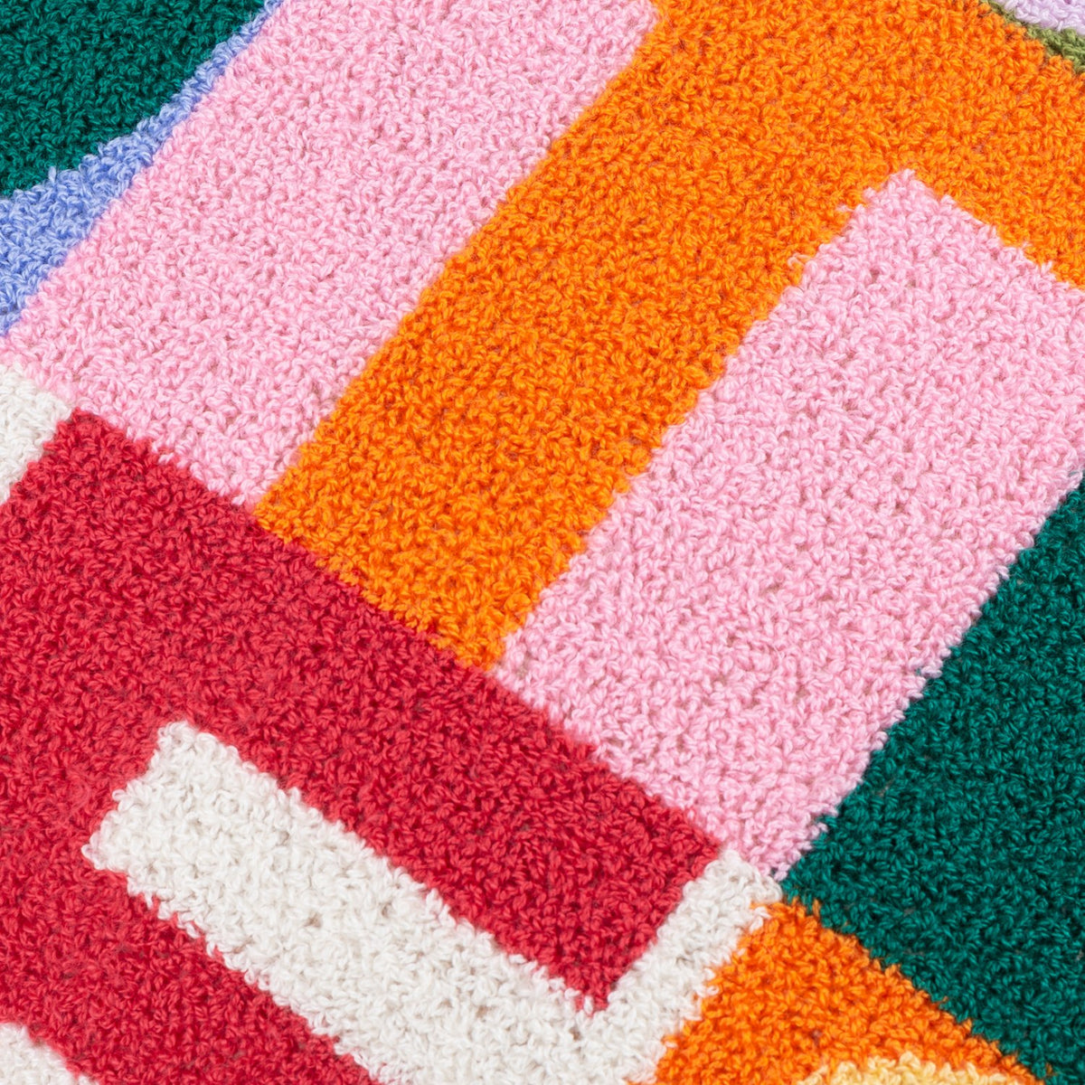 Close-up of the Good Times tufted polyester cushion showing micro-tufted boucle blocks in pink, orange, red, cream and green forming part of the lettered design.