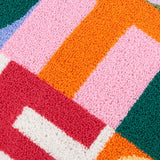 Close-up of the Good Times tufted polyester cushion showing micro-tufted boucle blocks in pink, orange, red, cream and green forming part of the lettered design.