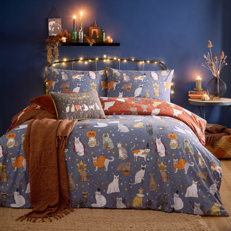 Halloween Pawty Reversible Duvet Cover Set on a bed in a dark blue bedroom, blue and rust cotton-blend fabric with costumed cats, stars, pumpkins and ghosts, styled with matching pillowcases.