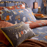Halloween Pawty reversible duvet cover set in blue and rust, shown on a bed with matching pillowcases and a cushion, printed with costumed cats among stars in a bedroom setting.