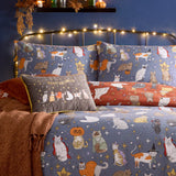 Halloween Pawty Reversible Animal Duvet Cover Set in blue, styled on a bed with matching pillowcases and a rust cushion printed with costumed cats, stars, and pumpkins, in a bedroom setting.