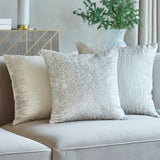 Hamlet Printed Polyester Cushion in Alabaster, a square cream cushion with a marbled metallic foil pattern, styled with two neutral cushions on a beige sofa.