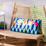 Happy Hour rectangular polyester cushion in navy and pale aqua geometric print with colourful cocktail illustrations, shown on a rattan bench beside a green throw.