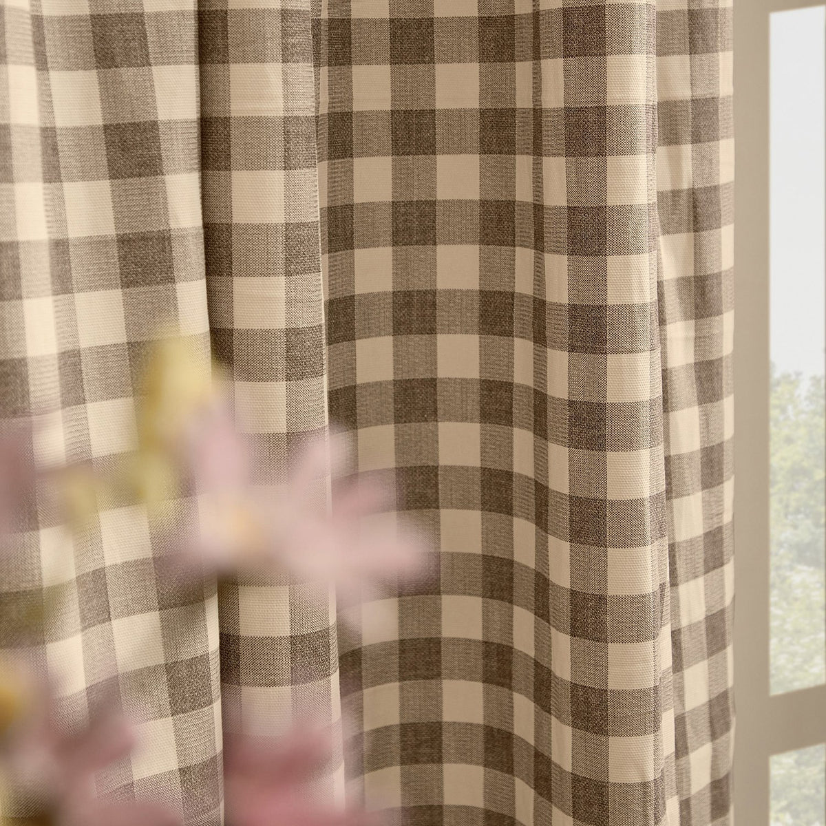 Harriet Gingham Cotton Pencil Pleat Curtains in buttermilk and chocolate brown check, shown pleated by a window with soft folds, styled with pink flowers in the foreground.