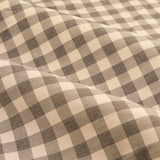 Close-up of Harriet Gingham cotton pencil pleat curtain fabric, showing a buttermilk and chocolate brown check pattern draped in soft folds.