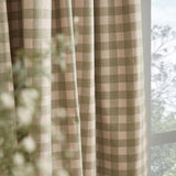 Harriet Gingham Cotton Pencil Pleat Curtains in pink and green check fabric, shown draped in folds beside a window with softly blurred foliage.