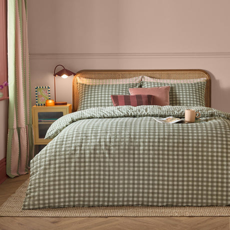 Harriet Gingham Cotton Check Duvet Cover Set in Baygreen/Mist dressed on a bed with matching pillowcases, cane headboard, and pink and burgundy accent cushions in a pink-walled bedroom.