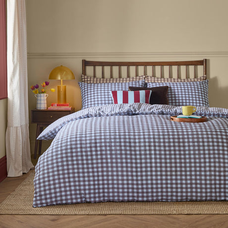 Harriet Gingham cotton check duvet cover set in blue and chocolate on a bed with matching pillowcases, striped and velvet cushions, in a bedroom setting.