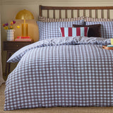 Harriet Gingham cotton duvet cover set in blue and chocolate check with seersucker texture, shown on a bed with matching pillowcases and striped accent cushions in a wooden-framed bedroom setting.