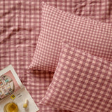 Harriet Gingham Cotton Check Duvet Cover Set in Burgundy/Blossom, showing seersucker-textured pillowcases and cover on a matching gingham bed, styled with a magazine and nail polish.
