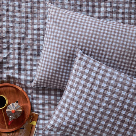 Harriet Gingham Cotton Pillowcase Pair in blue and chocolate check, shown on a matching seersucker duvet cover beside a wooden tray with coffee pot.