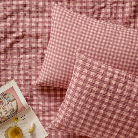 Harriet Gingham Cotton Pillowcase Pair in burgundy/blossom, shown on a matching seersucker gingham bedspread with textured checked fabric.