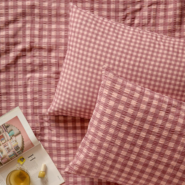 Harriet Gingham Cotton Pillowcase Pair in burgundy/blossom, shown on a matching seersucker gingham bedspread with textured checked fabric.