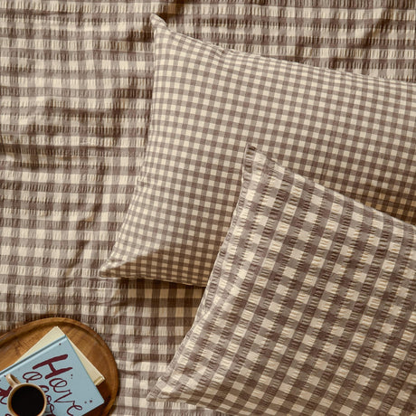 Harriet Gingham cotton pillowcase pair in buttermilk/chocolate check with seersucker texture, styled on matching bedding with a tray, mug, and book.
