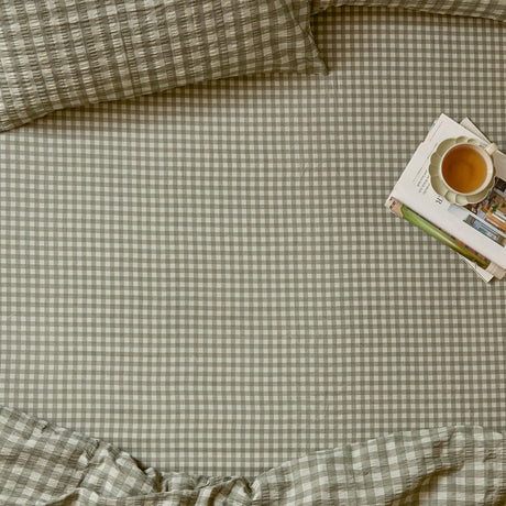 Harriet Gingham Check Cotton Fitted Sheet in baygreen/mist on a bed, showing the sage-and-cream check pattern with matching pillowcases, styled with a tray of books and tea.