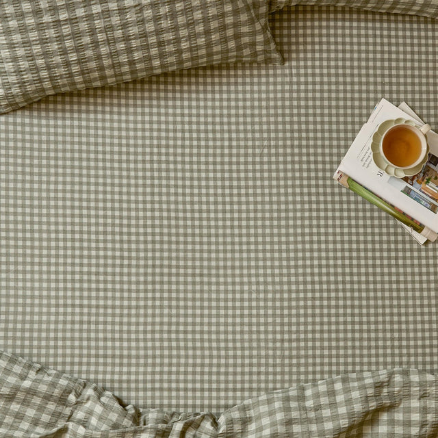 Harriet Gingham Check Cotton Fitted Sheet in baygreen/mist on a bed, showing the sage-and-cream check pattern with matching pillowcases, styled with a tray of books and tea.