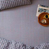 Harriet Gingham Check Cotton Fitted Sheet in blue/chocolate on a bed, with matching pillowcase, a wooden tray, coffee cup, and magazine nearby.