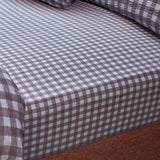Harriet Gingham Check Cotton Fitted Sheet on a mattress, showing a small brown and blue-white check pattern across the fabric with a fitted corner detail.
