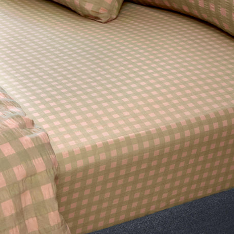 Harriet Gingham Check Cotton Fitted Sheet in pink and green, fitted over a mattress corner showing the woven check pattern, with matching pillowcase visible.