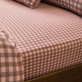 Harriet Gingham Check Cotton Fitted Sheet in rose and chocolate, showing the elasticated corner fitted over a mattress with matching pillowcases in the background.