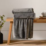 Harrow Plain Polyester Throw in charcoal, folded and draped over a wooden bench, showing its dense flannel fleece texture in a matt grey tone.