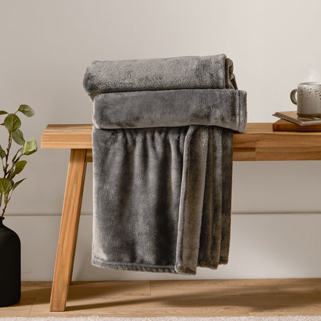Harrow Plain Polyester Throw in charcoal, folded and draped over a wooden bench, showing its dense flannel fleece texture in a matt grey tone.