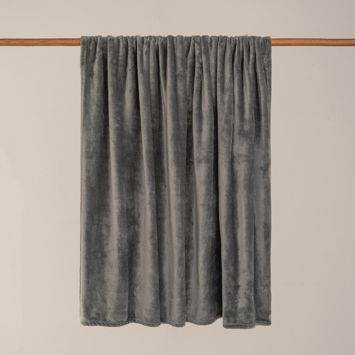 Harrow Plain Polyester Throw in charcoal, a flannel fleece throw with a smooth brushed grey finish, draped over a wooden rail against a plain light background.