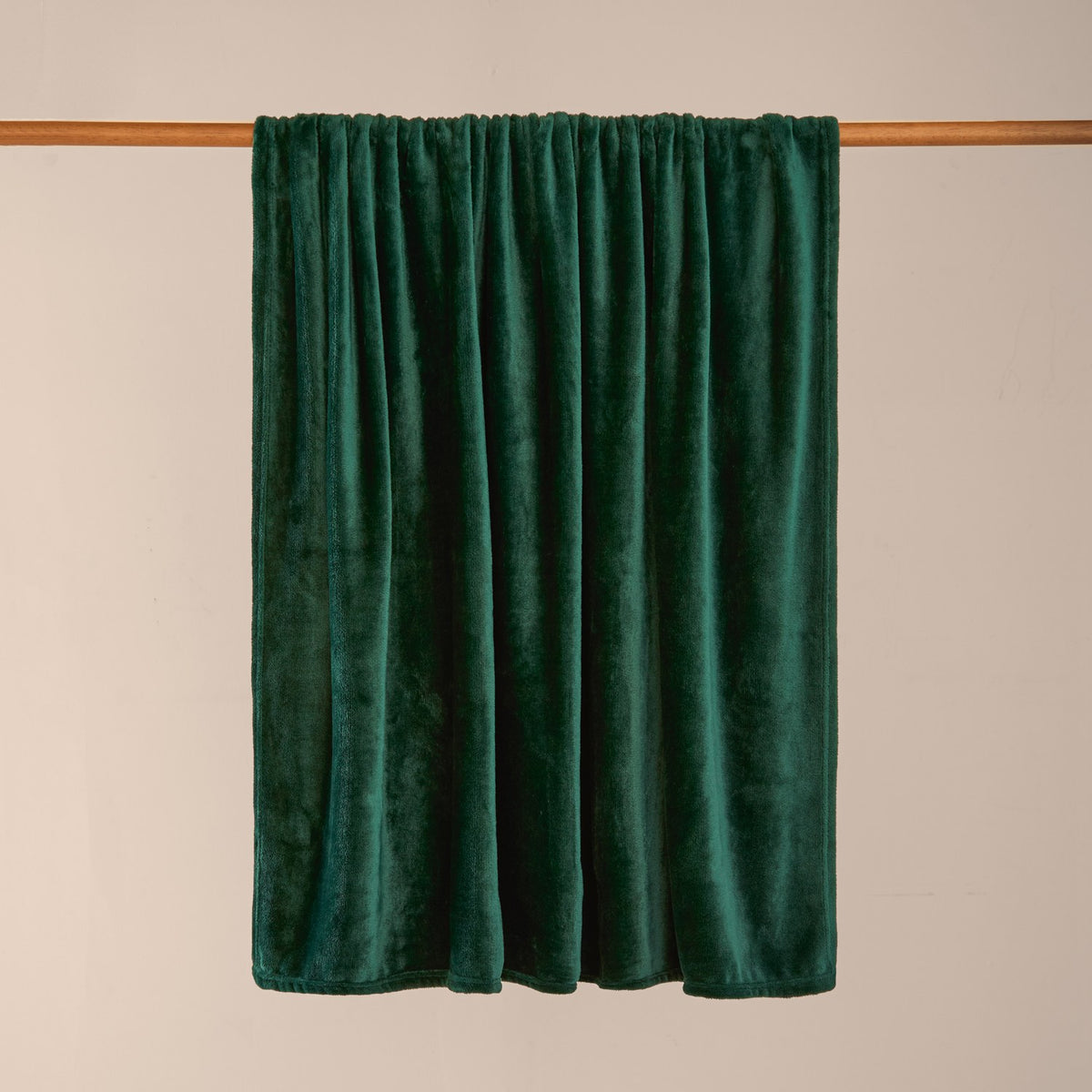 Harrow Plain Polyester Throw in emerald green, plain flannel fleece with a dense short pile, draped over a wooden pole against a plain neutral background.
