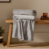 Harrow Plain Polyester Throw in grey, folded and draped over a wooden bench, showing its brushed flannel fleece texture in a living room setting.