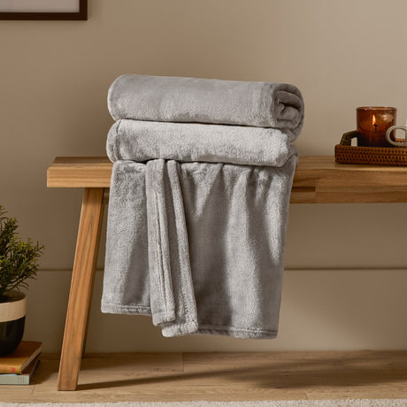 Harrow Plain Polyester Throw in grey, folded and draped over a wooden bench, showing its brushed flannel fleece texture in a living room setting.