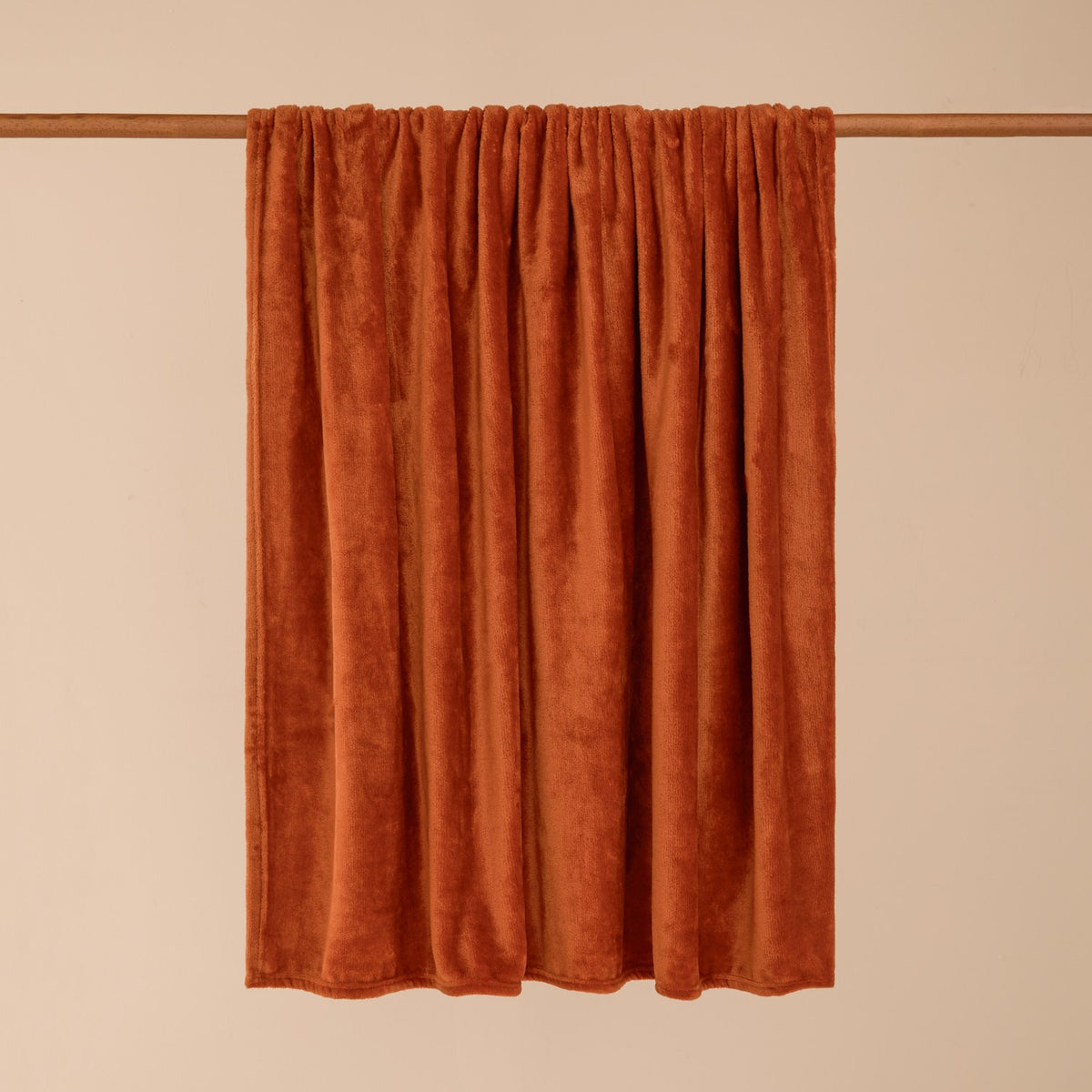 Harrow Plain Polyester Throw in rust orange, draped over a rail to show its flannel fleece texture, against a plain neutral background.