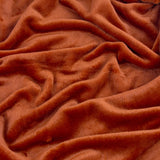 Harrow Plain Polyester Throw in rust orange, close-up of soft flannel fleece fabric shown with loose folds and creases.