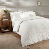 Harrison Stripe tufted white duvet cover set with matching pillowcases and a textured cushion, styled on a bed in a bedroom with a wooden nightstand.