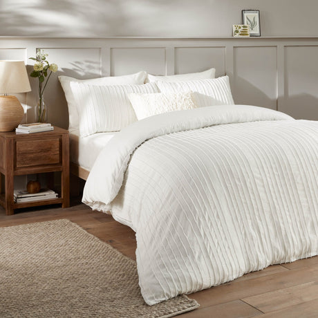 Harrison Stripe tufted white duvet cover set with matching pillowcases and a textured cushion, styled on a bed in a bedroom with a wooden nightstand.