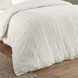 Harrison Stripe tufted polyester duvet cover set in white, showing raised striped texture on the bed in a bedroom setting with wooden flooring.