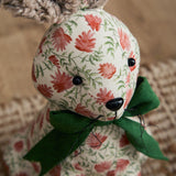 Close-up of Hattie hare-shaped door stop with bouclé ears, cream floral polyester face, black bead eyes and nose, and a green ribbed bow at the neck.