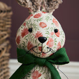 Hattie Polyester Door Stop hare-shaped design, close-up of face with bouclé ears, floral cream fabric, black button eyes and nose, green ribbed bow at neck.