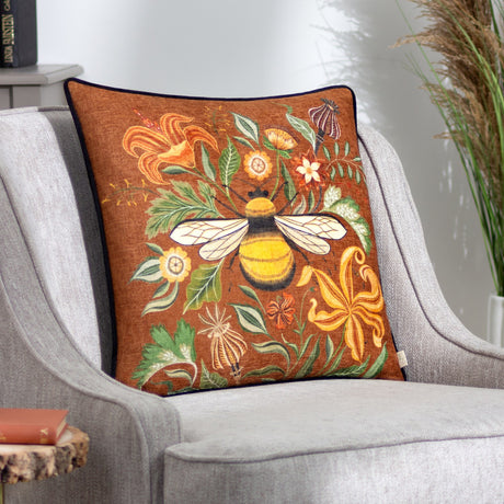 Hawthorn Bee square cushion in ginger printed velvet chenille with a bumblebee and floral design, black velvet reverse, styled on a grey armchair.