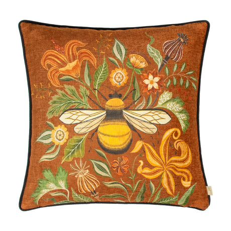 Square Hawthorn Bee cushion in ginger printed velvet chenille, featuring a bumblebee among orange lilies, ochre daisies and green foliage, with black piping, on a white background.