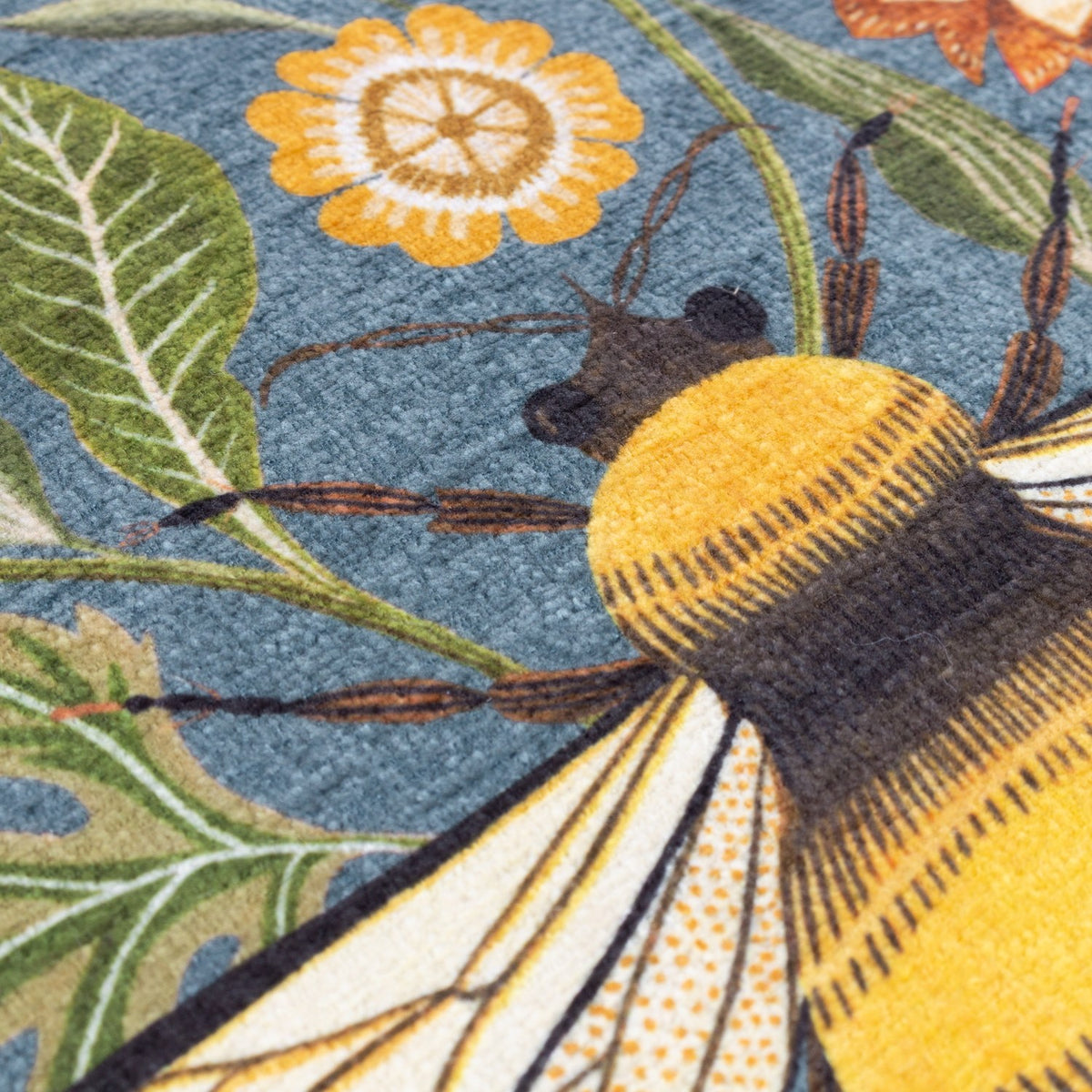 Close-up of the Hawthorn printed velvet chenille cushion in Petrol, showing a bumblebee and floral design in gold, orange and green on a textured chenille surface.