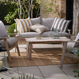 Hayle Reversible Cotton Cushion in chocolate and white stripes, styled on an outdoor sofa alongside a mustard striped cushion in a garden lounge setting.