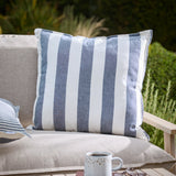 Hayle Reversible Cotton Cushion in navy, square with wide navy-and-white stripes, shown on a beige outdoor sofa in a garden setting.