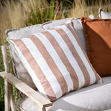 Hayle Reversible Cotton Cushion in pecan brown and white wide stripes, styled on an outdoor sofa with a rust cushion, set against a garden backdrop.
