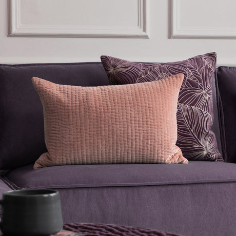 Haze Plain Velvet Cushion in coral, a rectangular quilted wave-textured bolster cushion on a purple sofa with a patterned cushion behind.
